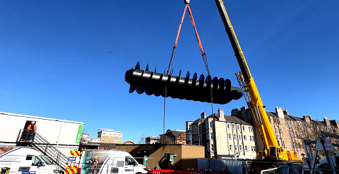 The screw pump is shown being hoisted into position by a large crane